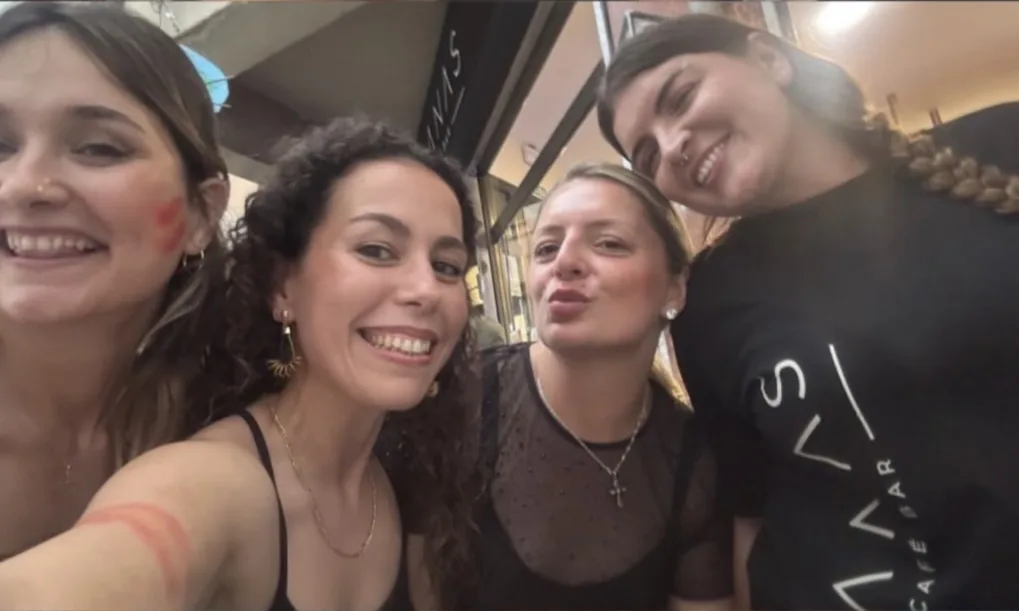 Grupo de amigas junto a la entrada de Manas, una con camiseta del bar
