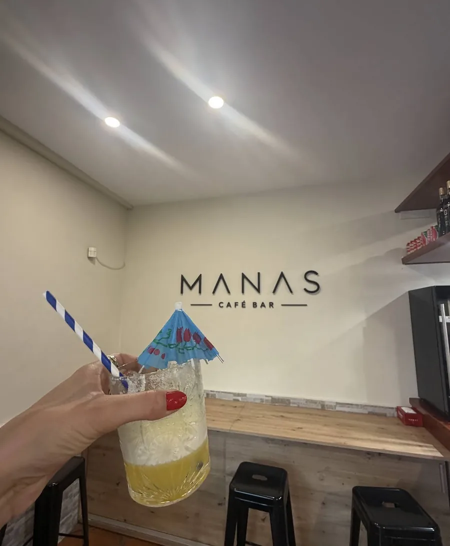 Cóctel de maracuyá con sombrilla azul frente al logo de Manas