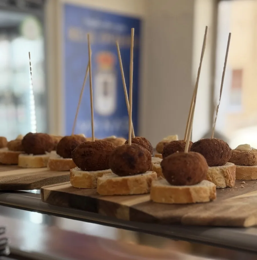 Pinchos de croqueta en la barra con el escudo del Real Oviedo al fondo